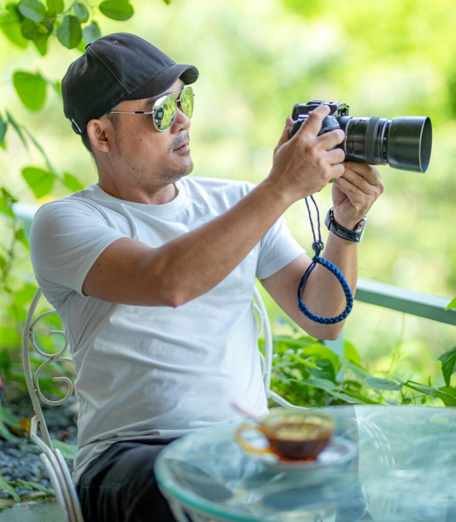 Man in white shirt using a camera outdoors, surrounded by greenery.